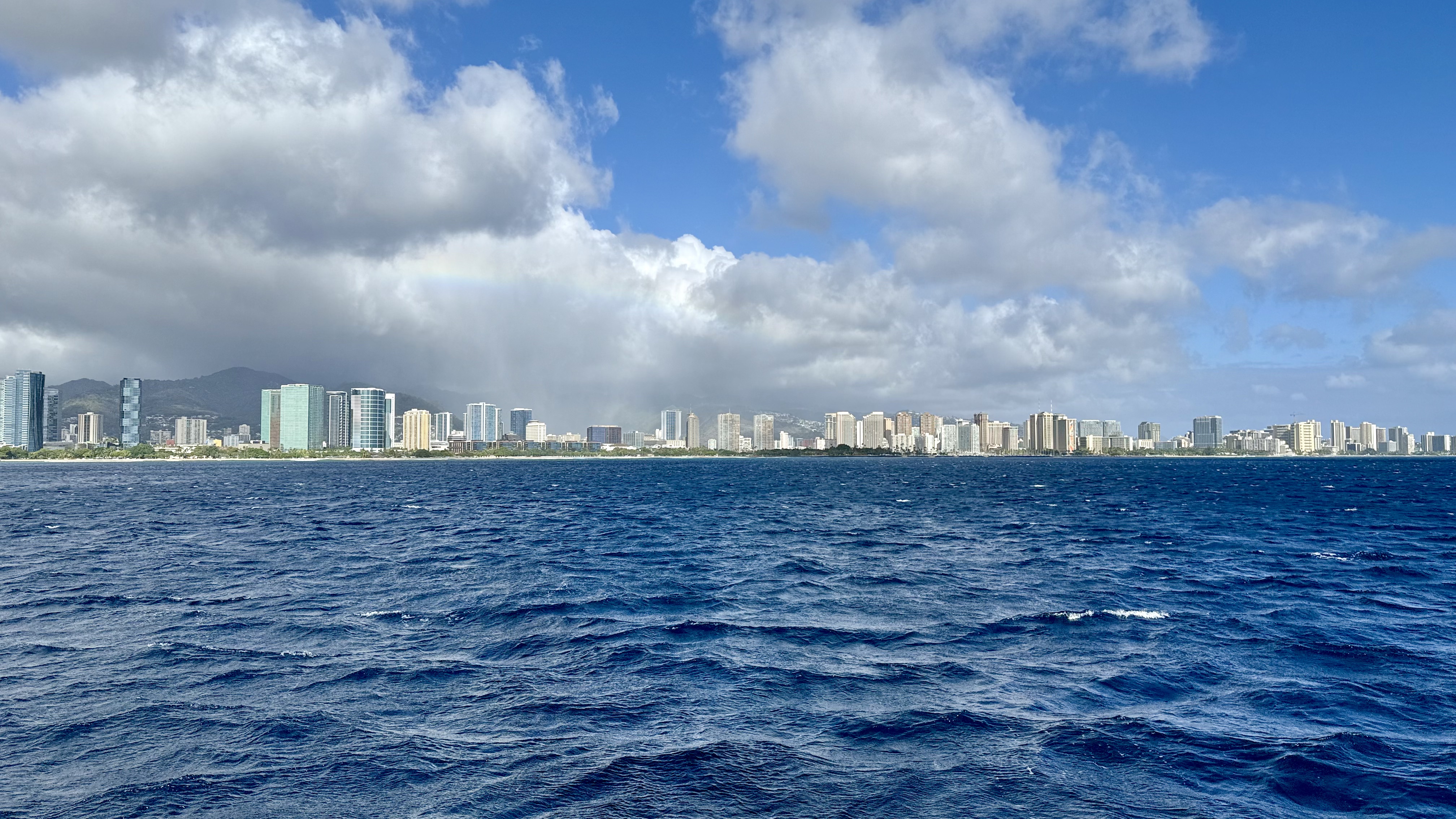 Waikiki and Ala Moana seen from the Makani - faint rainbow - a town being rained on. Illustrates sunny areas and raining towns at the same time on one image.