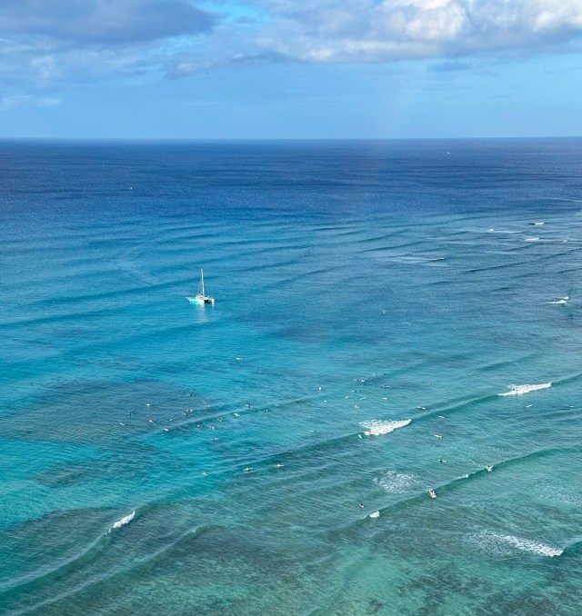 Faint rainbow over Canoes break at sunrise as Hawea catamaran arrives at Waikiki Shore